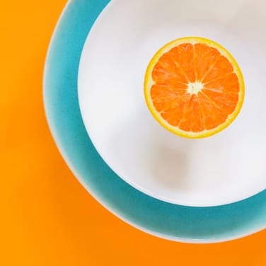 an orange in a white blue bordered plate with orange background